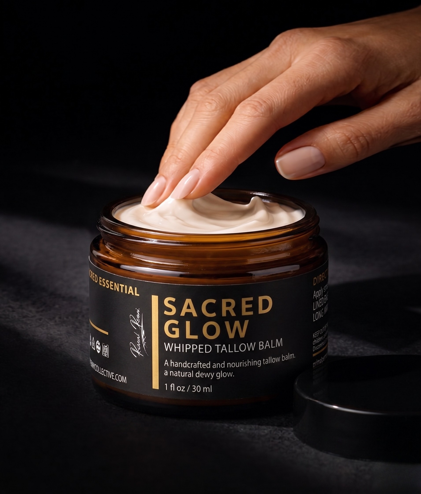 Hand applying whipped tallow balm from a jar labeled 'Sacred Glow' on a dark background